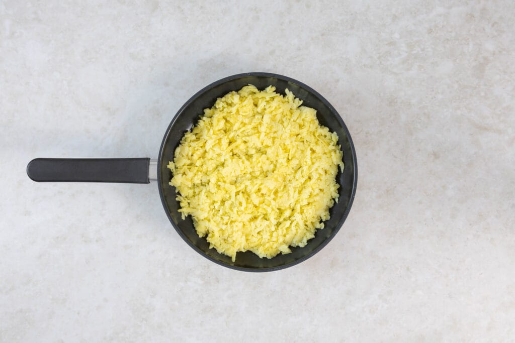 Geriebene Kartoffeln in der Pfanne, zu einem Fladen geformt für die knusprige Rösti