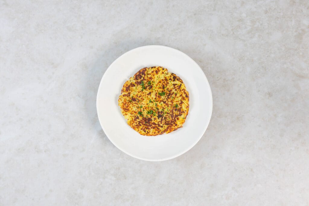 Fertig gebratene vegane Rösti, goldbraun und knusprig, mit Petersilie bestreut