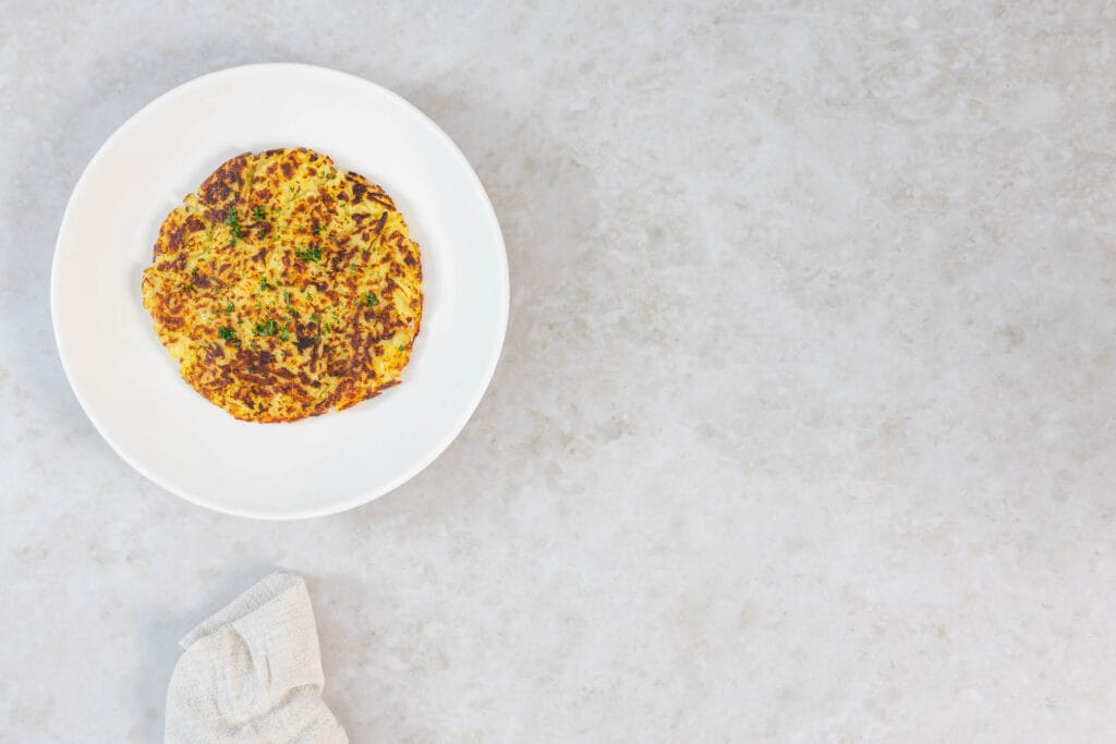 Goldbraune vegane Rösti ohne Ei auf einem Teller, mit Küchentuch daneben