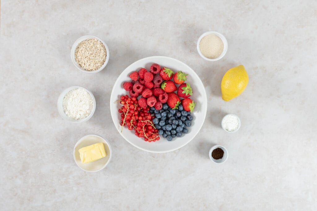 Zutaten für veganen Beeren-Crumble: gemischte Beeren, Haferflocken, Mehl, Rohrohrzucker, vegane Butter und Zitrone