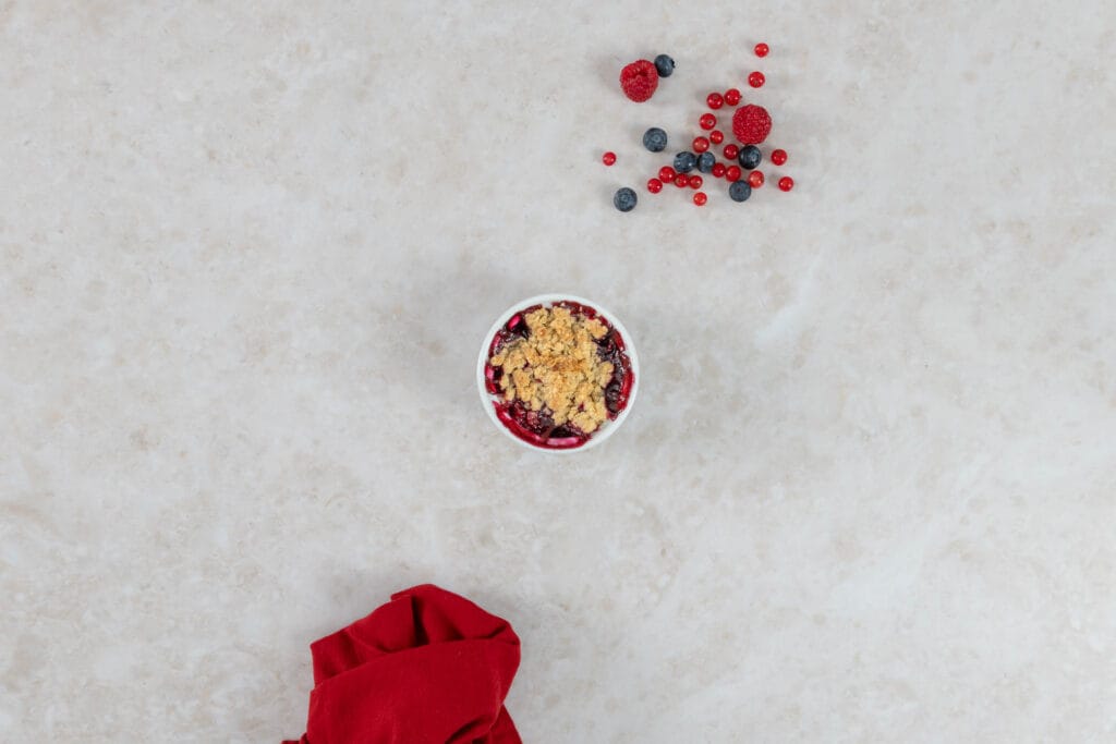Gebackener veganer Beeren-Crumble mit goldbrauner Haferflocken-Kruste und frischen Beeren daneben