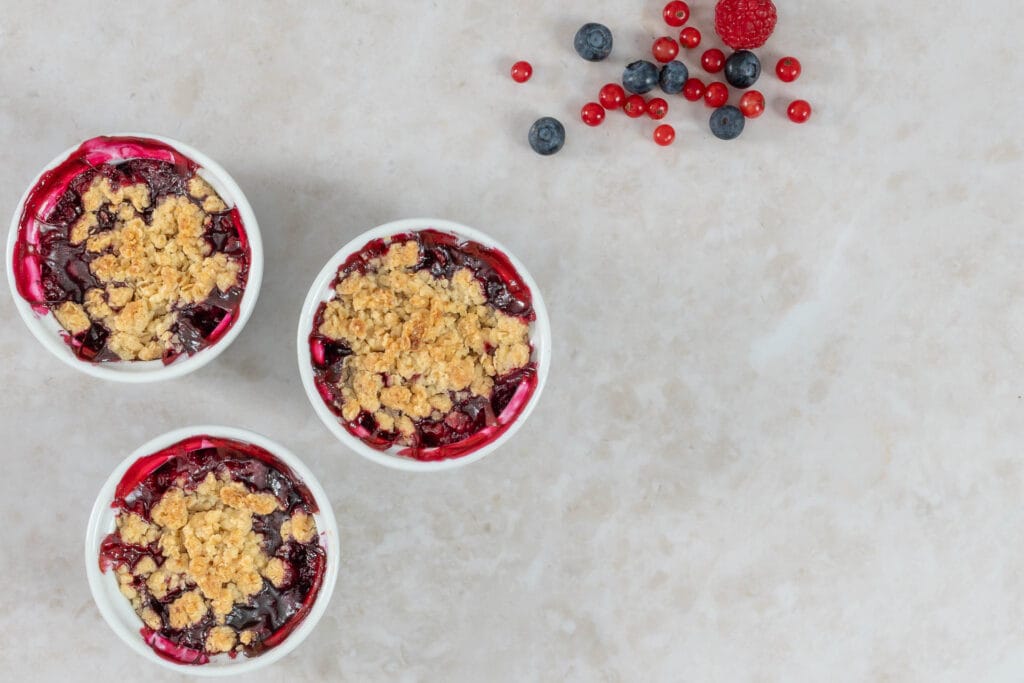 Drei vegane Beeren-Crumbles in Ofenschälchen, frisch gebacken mit knusprigen Streuseln