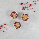 Drei Portionen Beeren-Crumble mit knuspriger Haferflocken-Kruste, umgeben von frischen Sommerbeeren