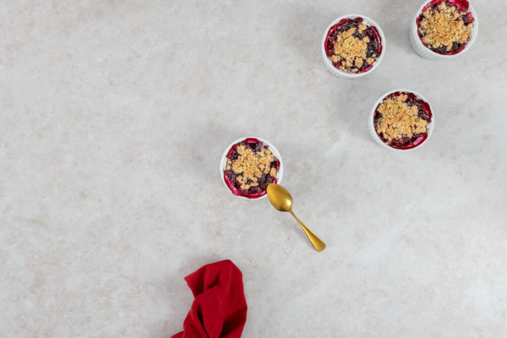 Vier Portionen Beeren-Crumble als Sommerdessert mit Löffel und roter Stoffserviette