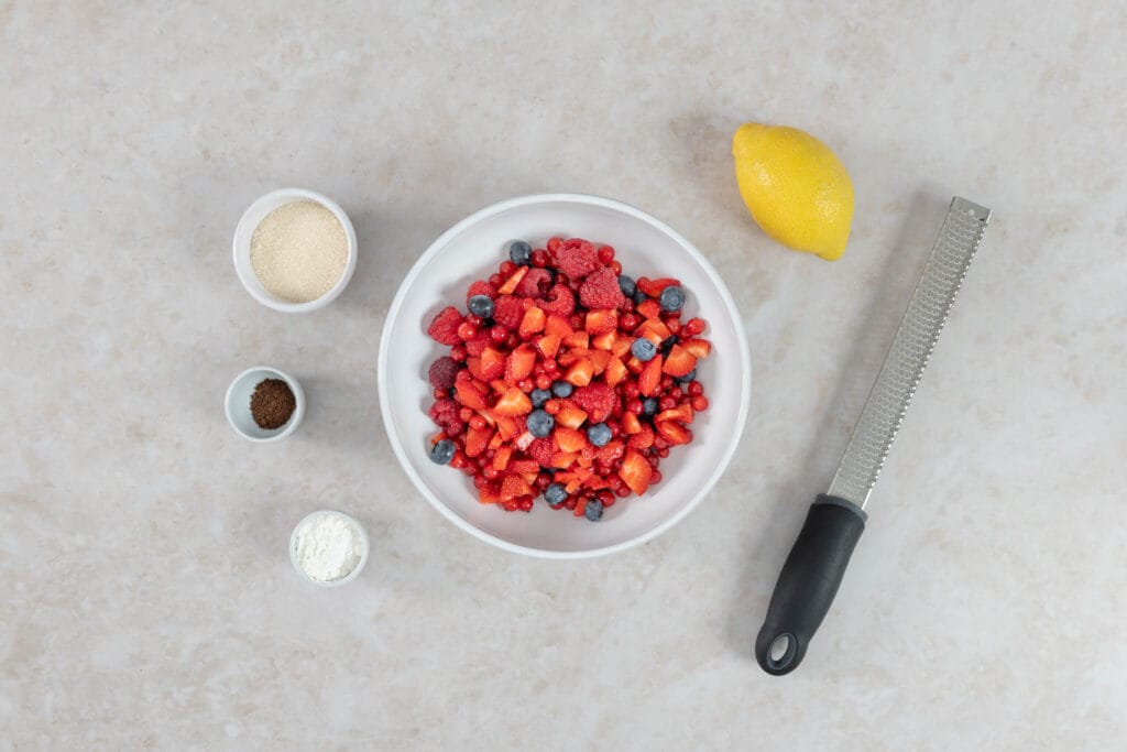 Beeren für den Crumble mit Zucker, Maisstärke und Zitrone, daneben eine Zitronenreibe