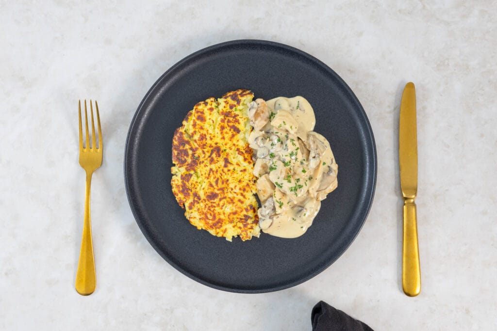 Veganes Zürcher Geschnetzeltes mit knuspriger Rösti auf einem dunklen Teller angerichtet