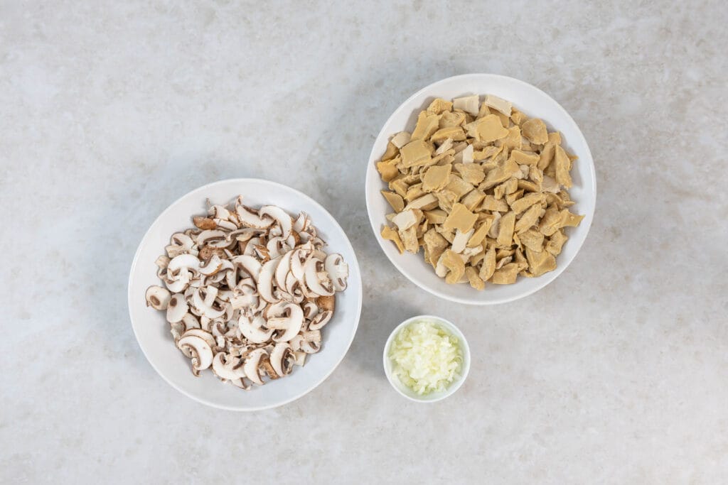 Geschnittene Champignons, gehackte Zwiebel und mundgerechtes veganes Geschnetzeltes bereit zum Anbraten