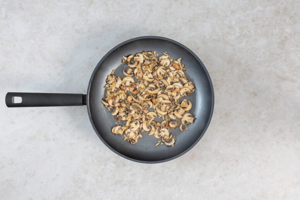 Champignons und Zwiebeln dünsten in der Pfanne für die vegane Rahmsauce