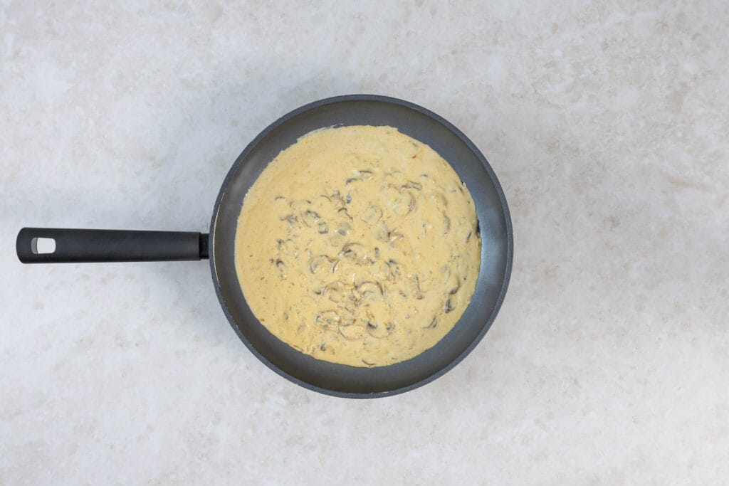 Cremige vegane Rahmsauce mit Champignons köchelt in der Pfanne