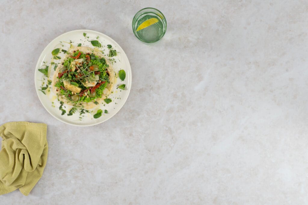 Veganes Fladenbrot mit Erbsencreme, garniert mit Kräutern und Pinienkernen, dazu ein Glas Zitronenwasser