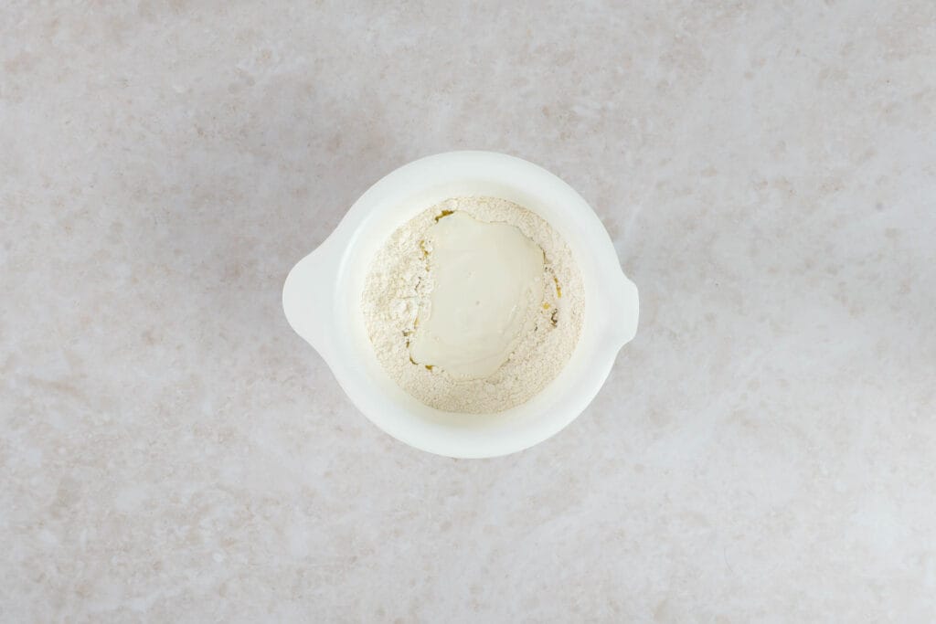 Veganer Joghurt und Mehl in einer Schüssel, bereit zum Kneten des Fladenbrotteigs
