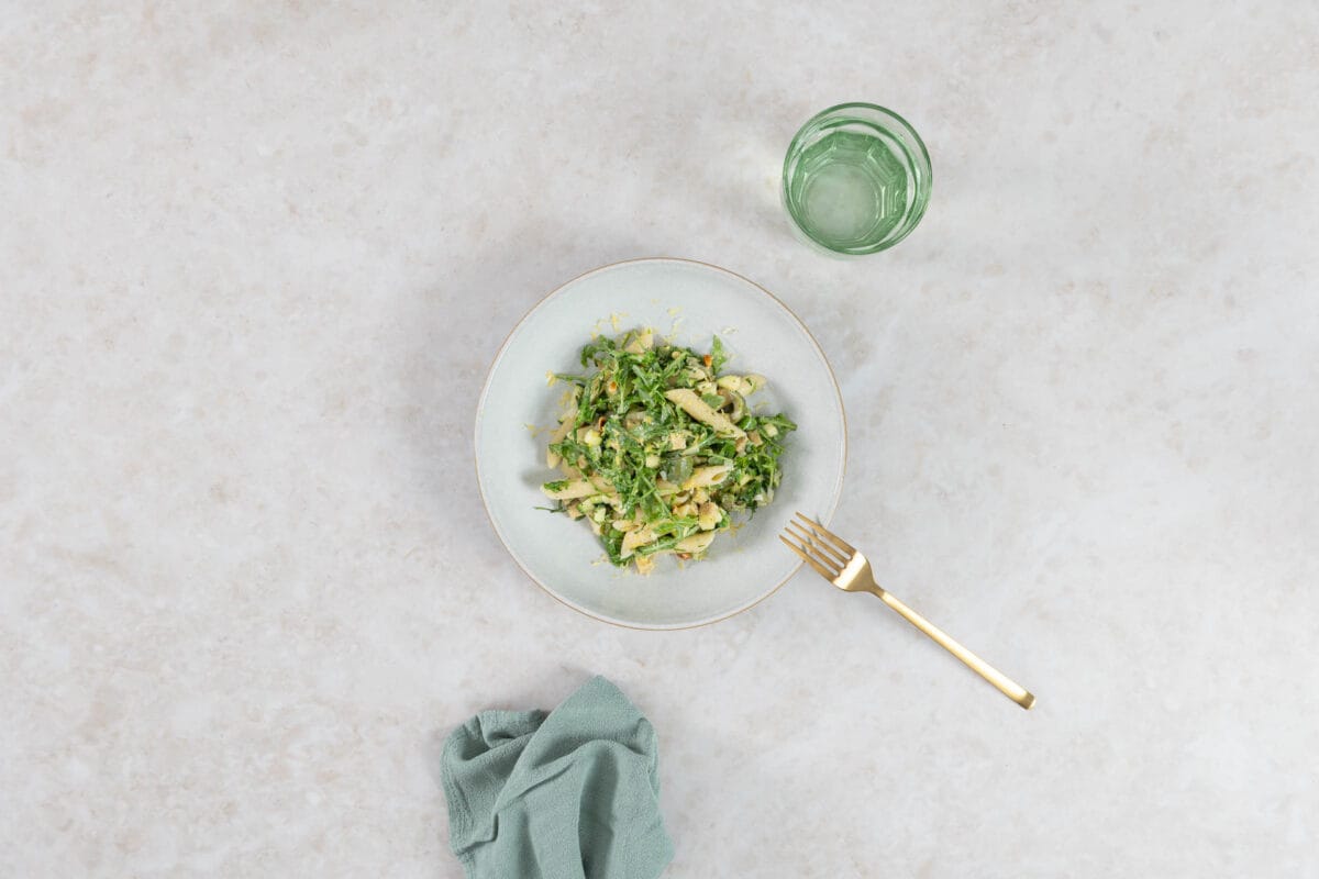 Veganer grüner Pastasalat mit Knuspertofu, serviert mit Wasserglas und goldener Gabel