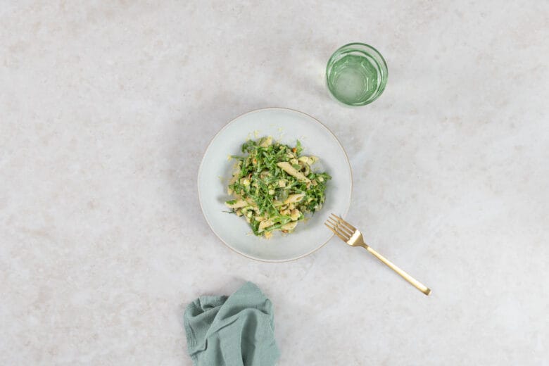 Veganer grüner Pastasalat mit Knuspertofu, serviert mit Wasserglas und goldener Gabel