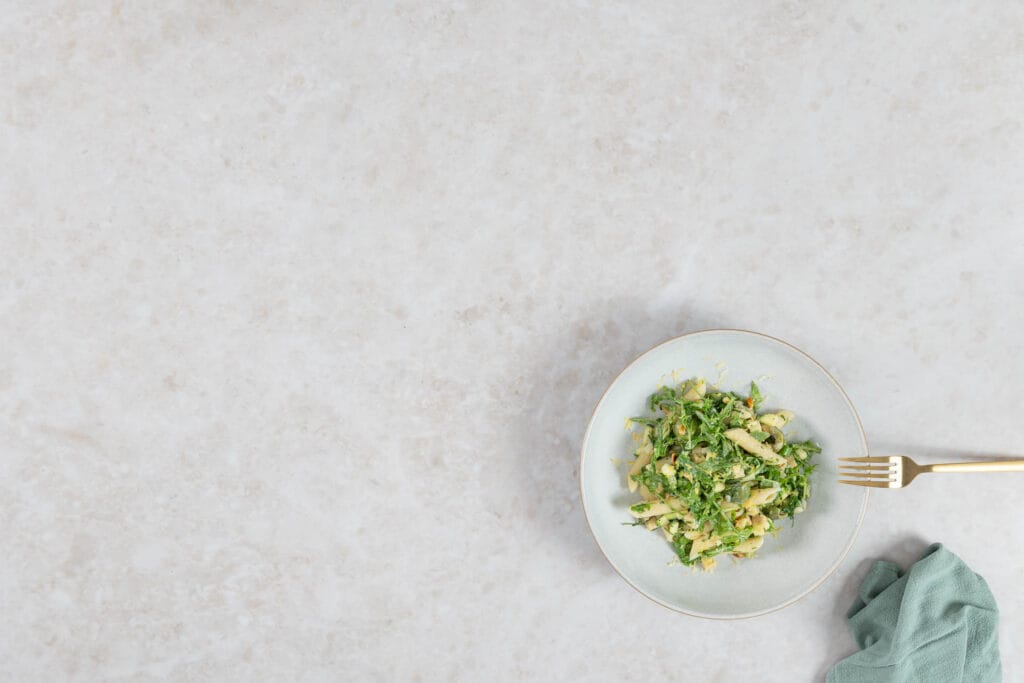 Grüner Pastasalat mit Rucola und Penne, sommerlich angerichtet mit goldener Gabel