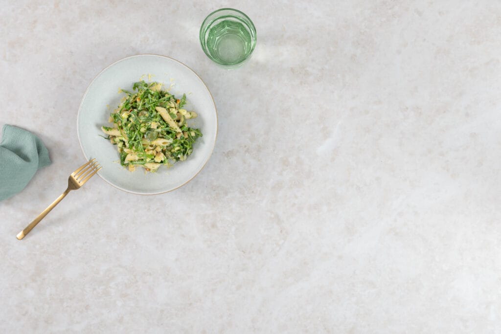 Cremiger grüner Pastasalat mit Kräuter-Joghurt-Dressing, angerichtet mit Serviette und Wasserglas
