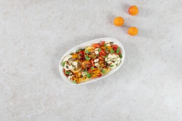 Grillierter Aprikosensalat mit gegrillten Aprikosen, bunten Tomaten und veganer Ricottacreme auf einer weissen Platte, daneben frische Aprikosen