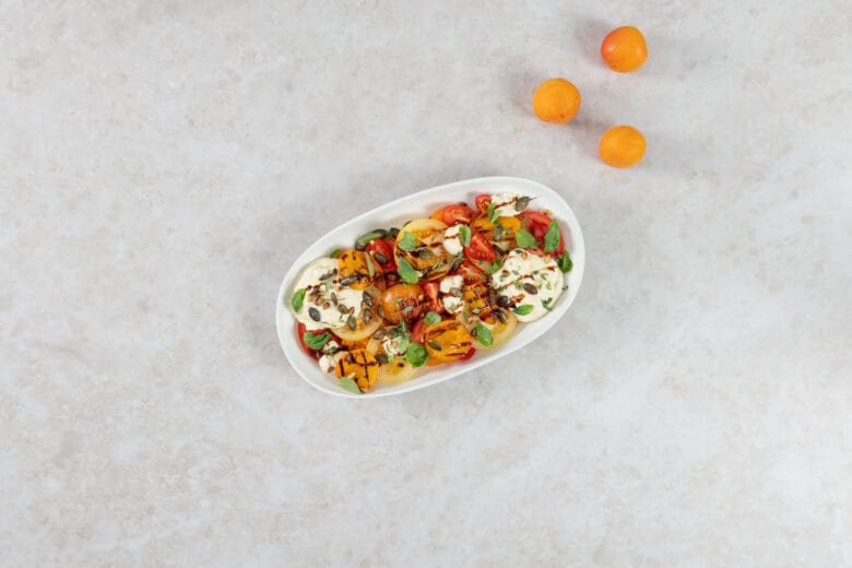 Grillierter Aprikosensalat mit gegrillten Aprikosen, bunten Tomaten und veganer Ricottacreme auf einer weissen Platte, daneben frische Aprikosen
