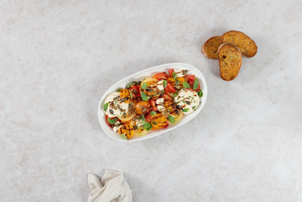 Grillierter Aprikosensalat mit bunten Tomaten und veganem Ricotta, daneben drei Scheiben geröstetes Knoblauchbrot
