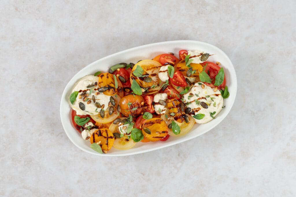 Grillierter Aprikosensalat mit gegrillten Aprikosen, bunten Tomaten, veganem Ricotta, Kürbiskernen und Basilikum, beträufelt mit Aceto Balsamico Crema