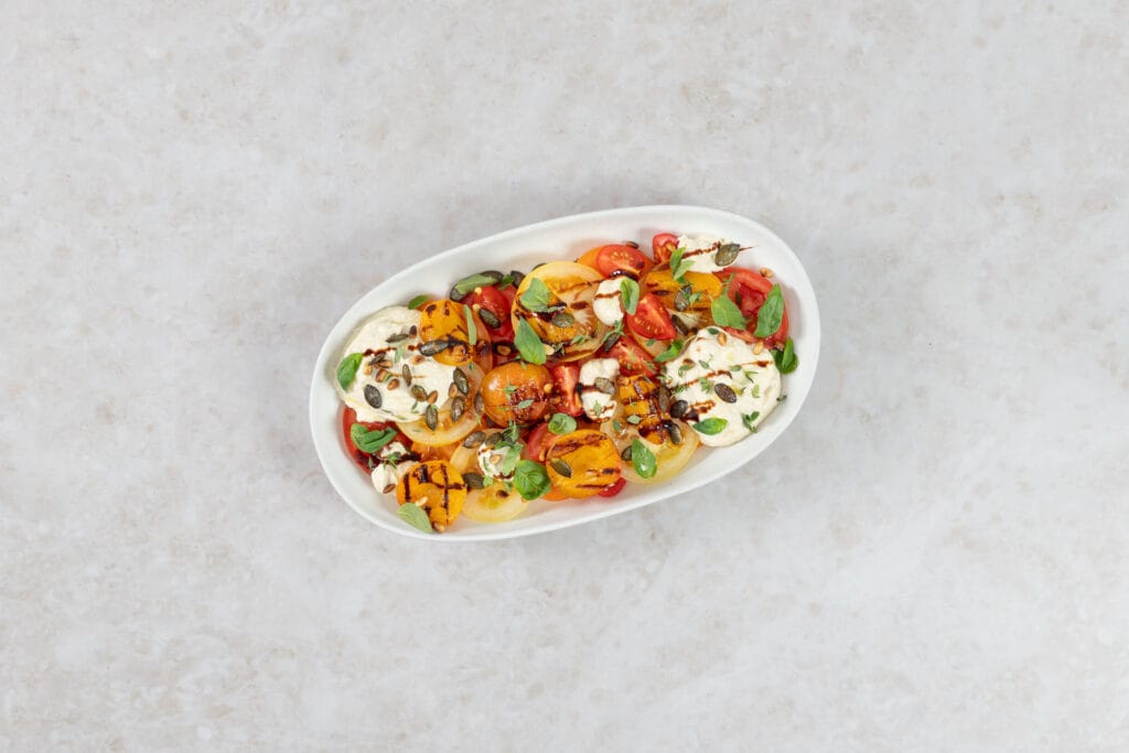 Veganes Sommergericht mit grillierten Aprikosen, bunten Tomaten und cremigem veganem Ricotta auf ovaler Platte von oben
