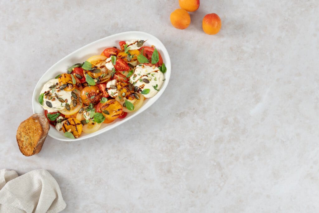 Leichtes Sommergericht mit gegrillten Aprikosen, bunten Tomaten und veganem Ricotta, dazu Knoblauchbrot und frische Aprikosen