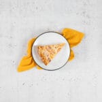 Stück der veganen Aprikosenwähe ohne Ei auf weissem Teller mit gelber Serviette, sommerlich angerichtet
