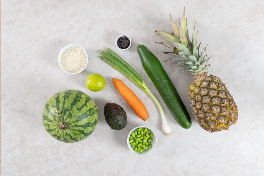 Zutaten für die vegane Wassermelonen-Thunfisch Poké Bowl mit Wassermelone, Sushi-Reis, Avocado, Ananas, Gurke, Karotte, Edamame und Nori-Flocken