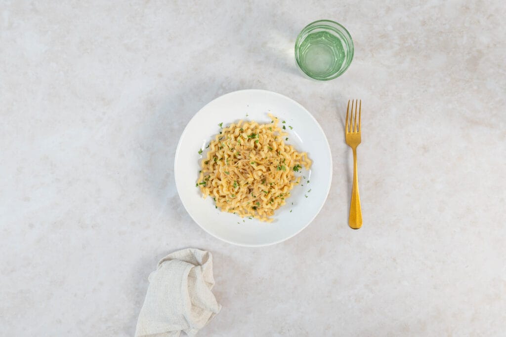Vegane Caramelized Onion Pasta serviert mit Wasserglas, Leinenserviette und goldenem Besteck