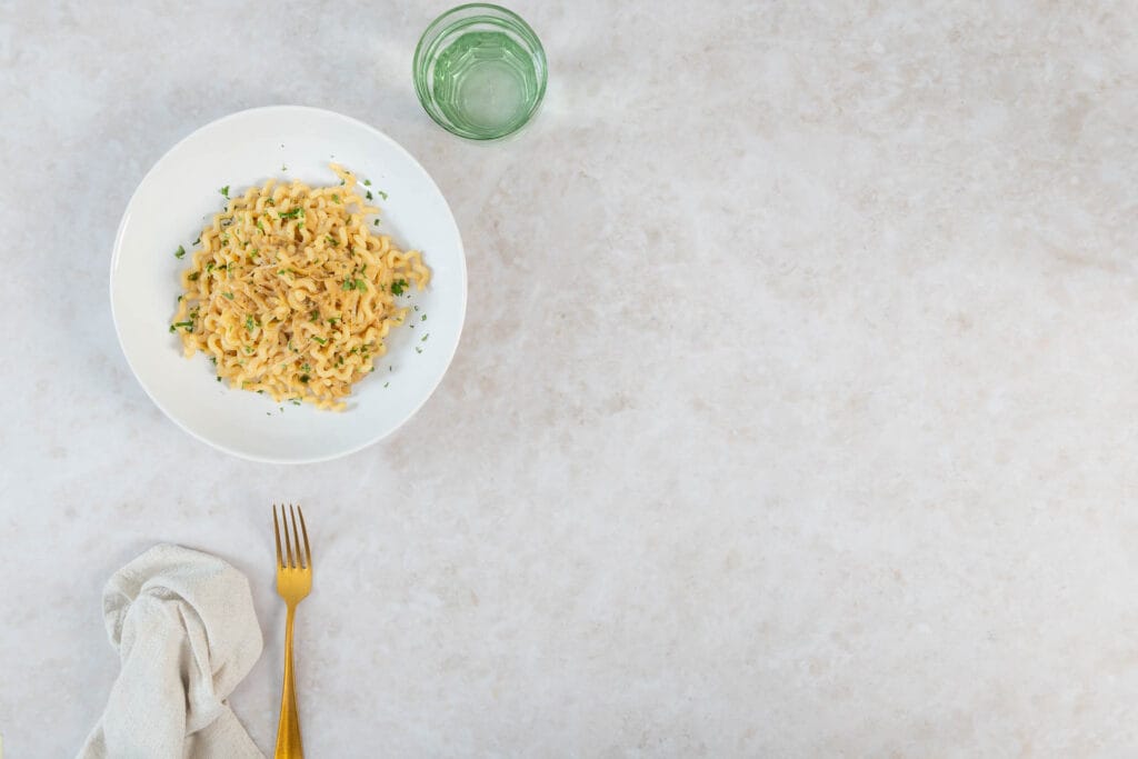Teller mit karamellisierter Zwiebel-Pasta, Wasserglas und Leinenserviette auf Marmor
