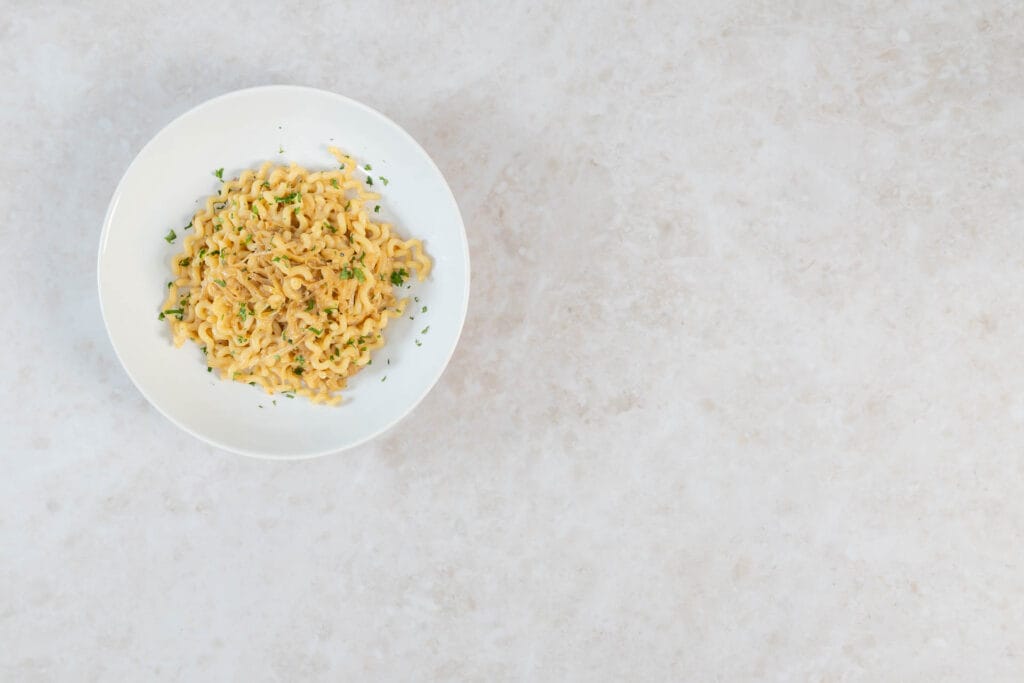 Kleine Portion vegane Zwiebel-Pasta mit Petersilie auf weissem Teller