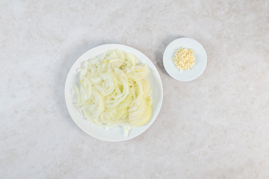 In feine Streifen geschnittene Zwiebeln und gehackter Knoblauch auf weissen Tellern vorbereitet