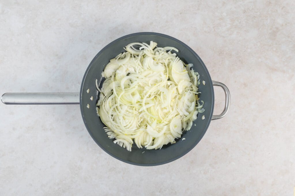 Rohe Zwiebelstreifen in Olivenöl und Butter in der grossen Bratpfanne zu Beginn des Karamellisierens