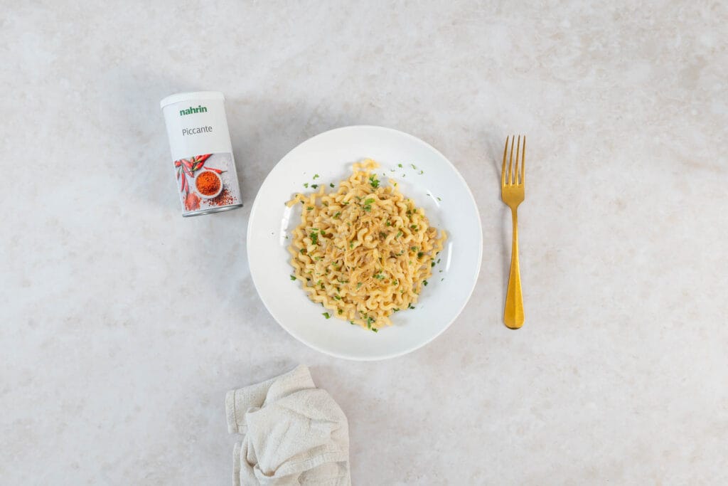 Angerichtete vegane Zwiebel-Pasta neben der Nahrin Piccante Dose und goldener Gabel
