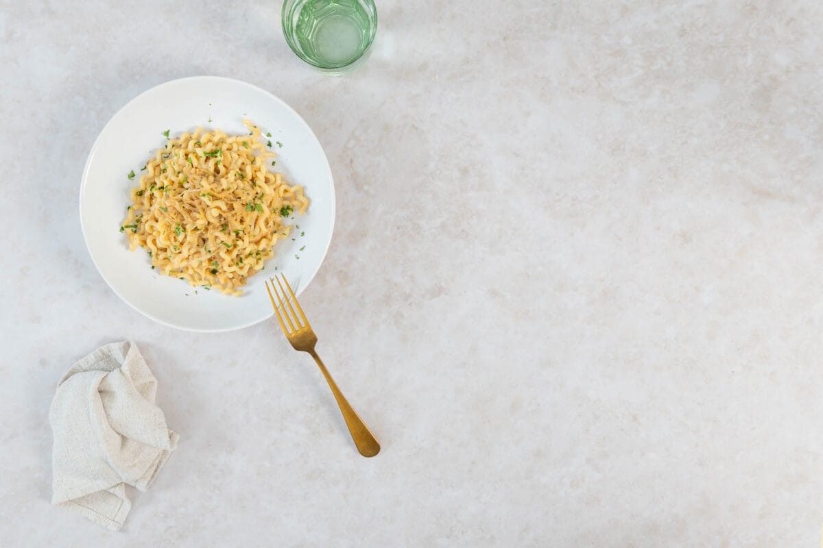 Vegane karamellisierte Zwiebel-Pasta mit Petersilie auf weissem Teller mit goldener Gabel