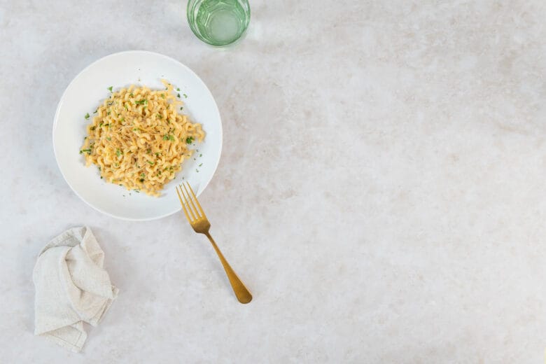 Vegane karamellisierte Zwiebel-Pasta mit Petersilie auf weissem Teller mit goldener Gabel