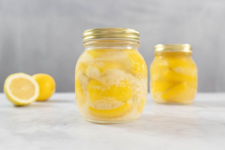 Zwei Gläser mit selbst eingelegten Zitronen, daneben eine halbierte Zitrone
