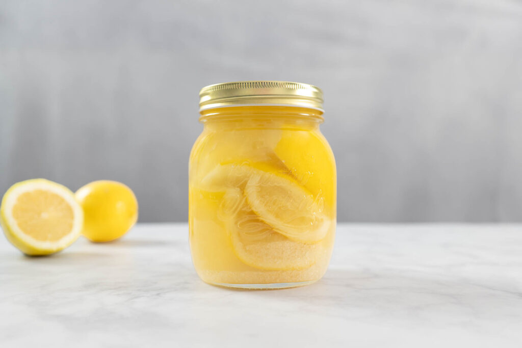 Fertig gereifte Salzzitronen mit goldgelber Lake im Glas neben frischen Zitronen
