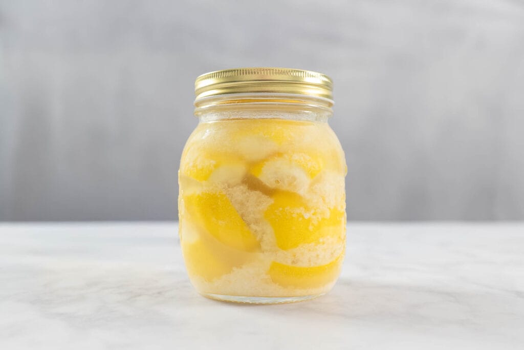 Eingelegte Zitronen im Glas mit grobem Meersalz, frisch angesetzt zum Fermentieren