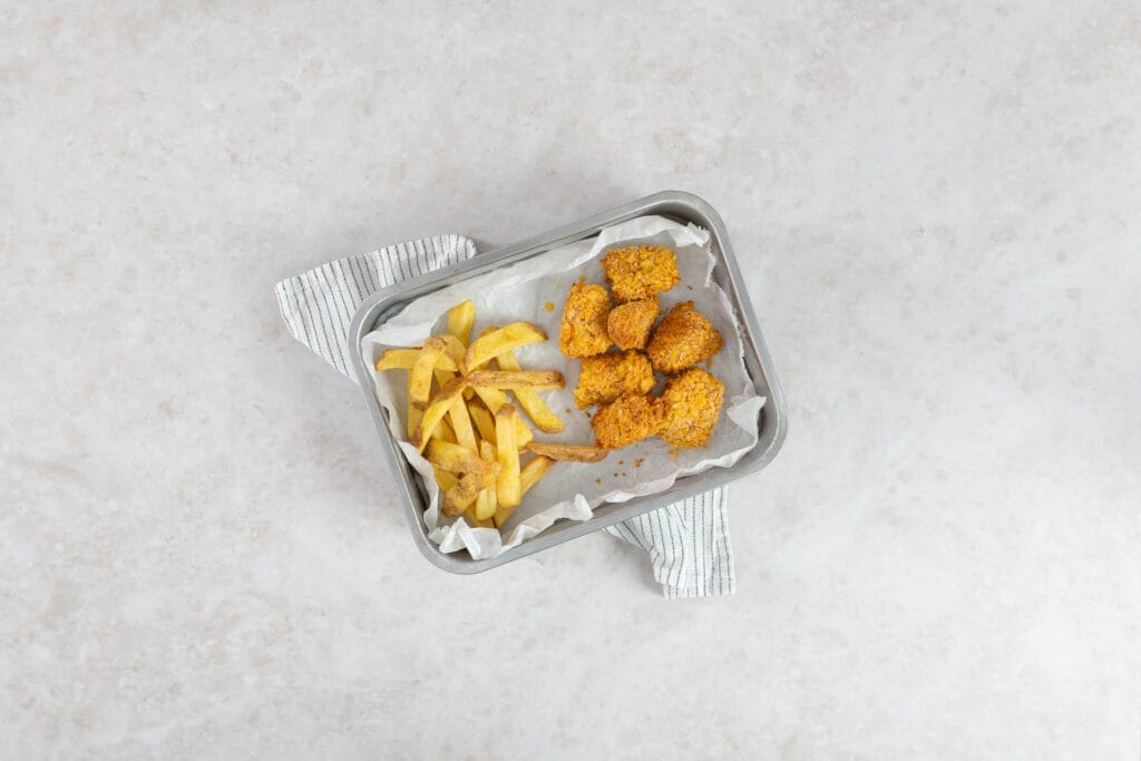 Vegane Tofu Nuggets aus dem Airfryer mit Pommes auf einem Blech mit Backpapier