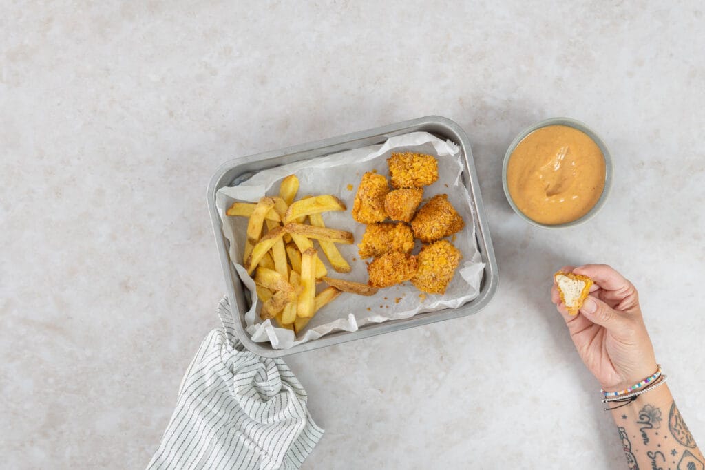 Angebissene knusprige vegane Tofu Nuggets aus dem Airfryer zeigen das zarte Innere, dazu Pommes und Dip