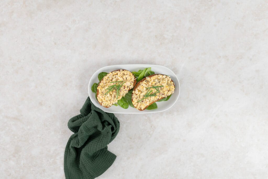 Veganer Thunfischsalat ohne Fisch auf Ruchbrot, serviert auf einer weissen Platte mit grüner Serviette