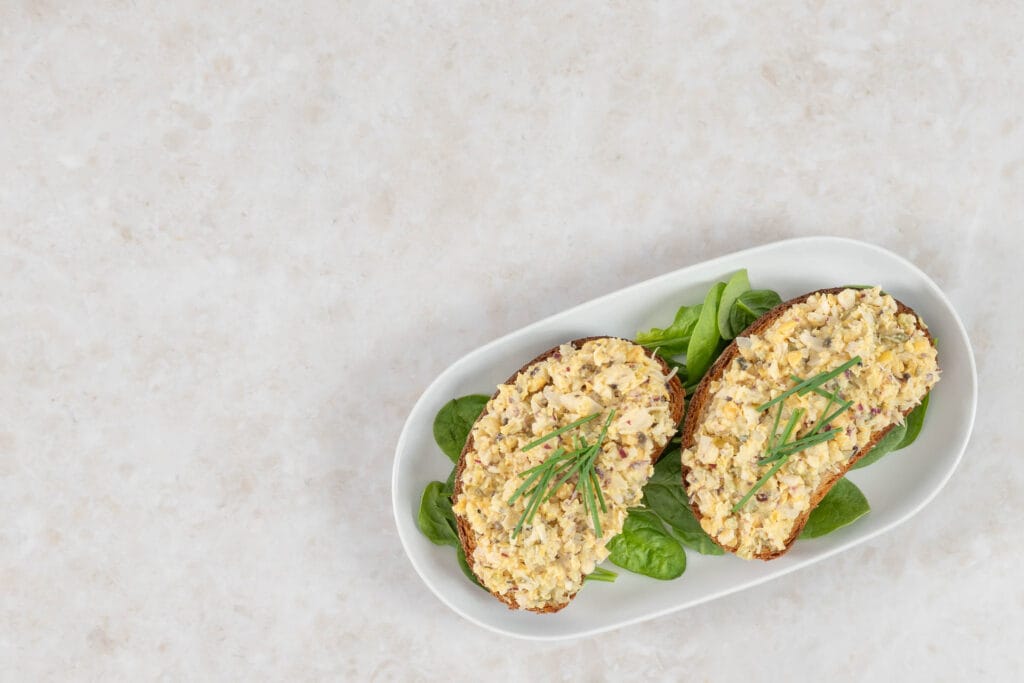 Veganer Thonsalat auf zwei Broten mit Spinatblättern, schräg von oben
