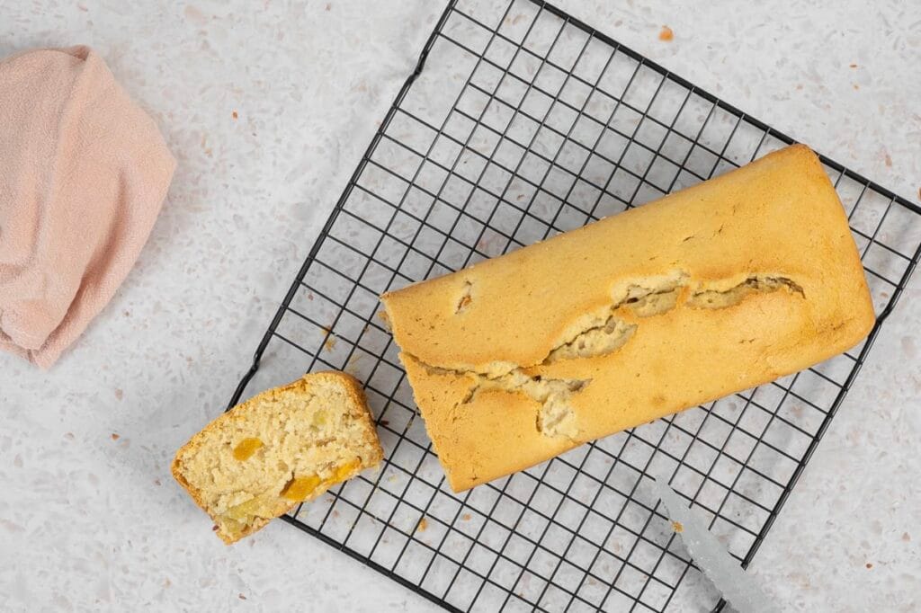 Angeschnittenes veganes Fruchtsalatcake von oben, die erste Scheibe zeigt die saftige Krume mit Pfirsich- und Ananasstücken und Serviette