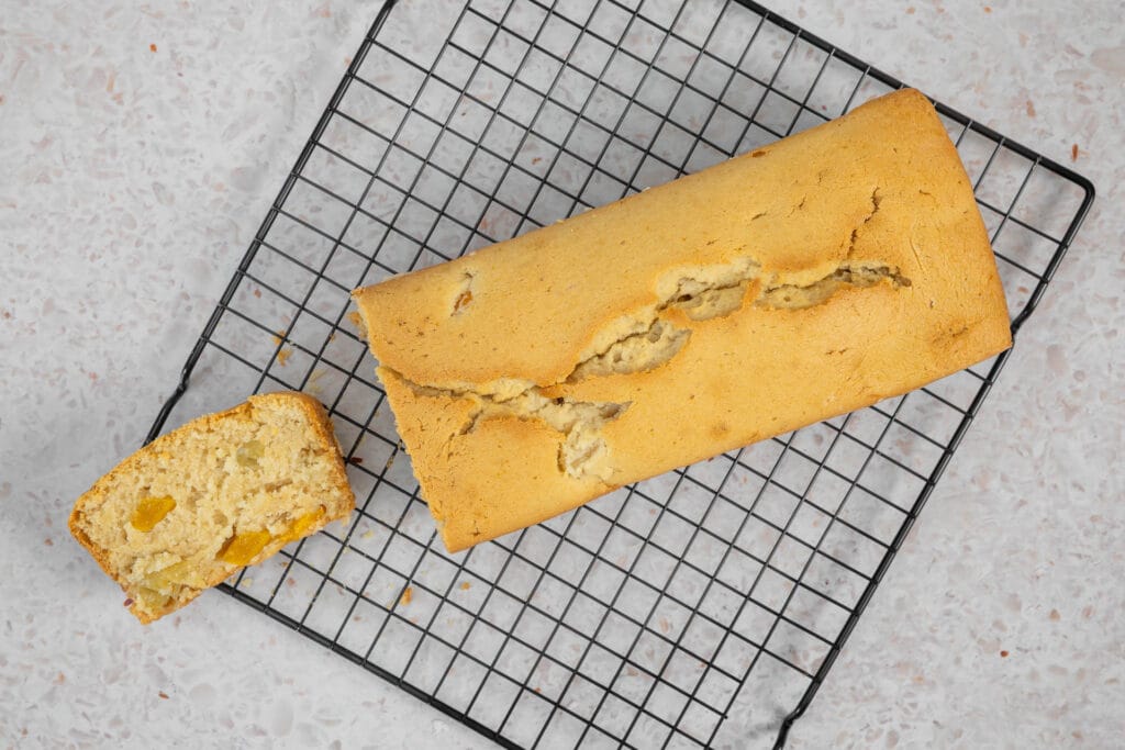 Angeschnittenes veganes Fruchtsalatcake von oben, die erste Scheibe zeigt die saftige Krume mit Pfirsich- und Ananasstücken