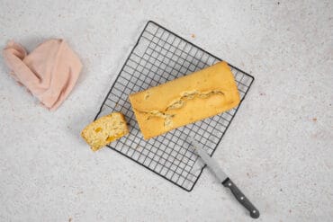 Veganer Fruchtcocktail-Kuchen auf dem Auskühlgitter, daneben eine abgeschnittene Scheibe und ein Messer