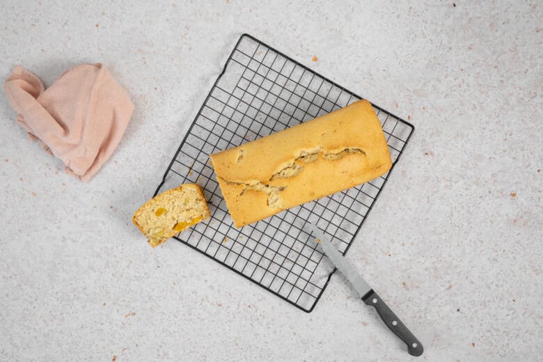 Veganer Fruchtcocktail-Kuchen auf dem Auskühlgitter, daneben eine abgeschnittene Scheibe und ein Messer