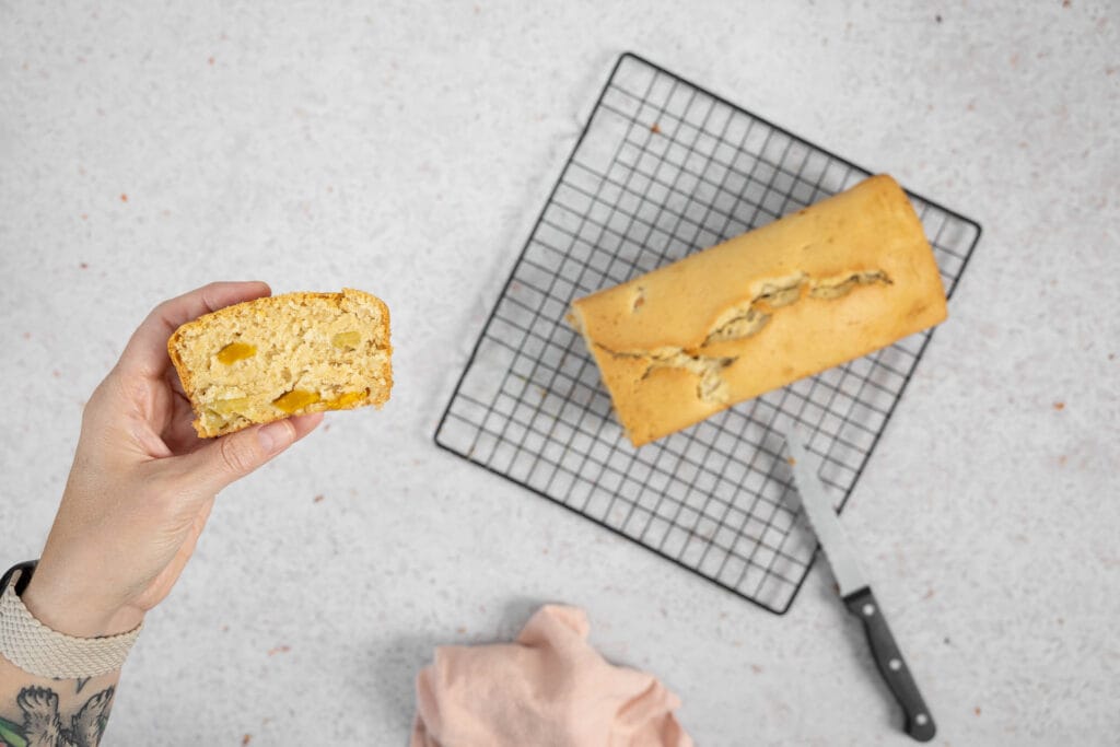 Aufgeschnittenes veganes Fruchtsalatcake, eine Scheibe in der Hand mit sichtbaren Fruchtstücken aus der Dose