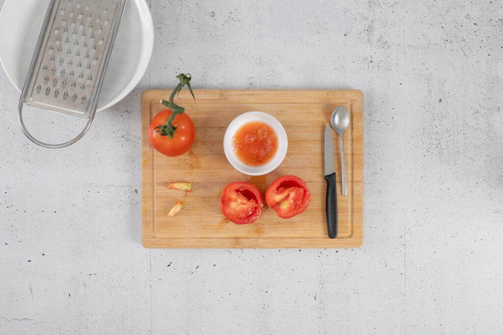 Halbierte Tomaten mit entfernten Kernen, daneben Teelöffel und Röstiraffel