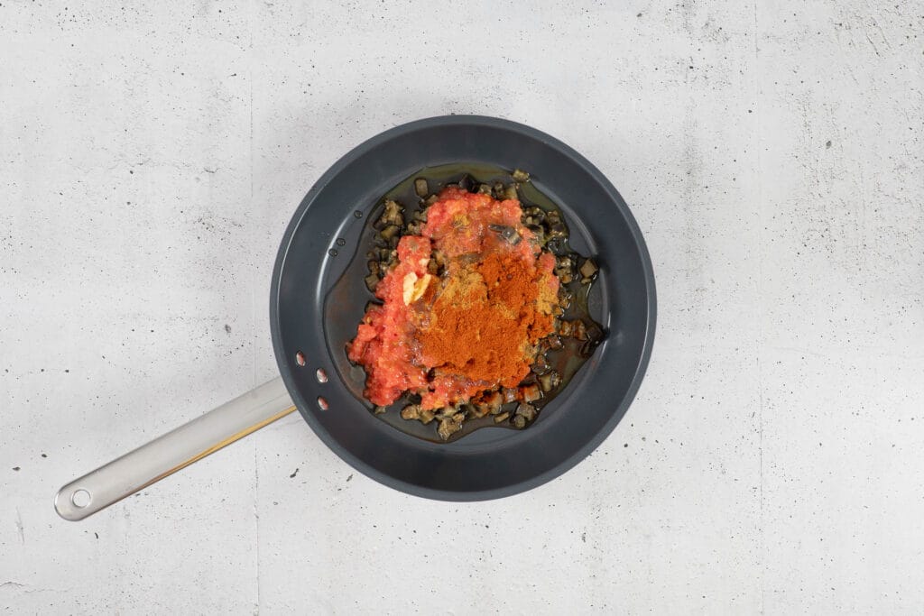Auberginen, geriebene Tomaten, Knoblauch, Kreuzkümmel und Paprika mit Olivenöl in der kalten Bratpfanne