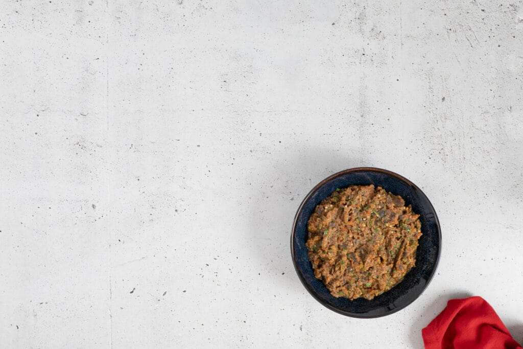 Marokkanischer Auberginensalat in einer dunkelblauen Schale auf hellem Betonuntergrund
